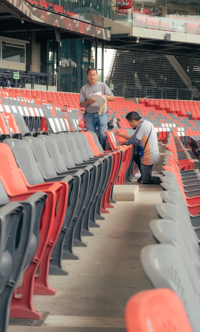 cta-bg Two workers cleaning empty stadium seats, ensuring cleanliness before events.